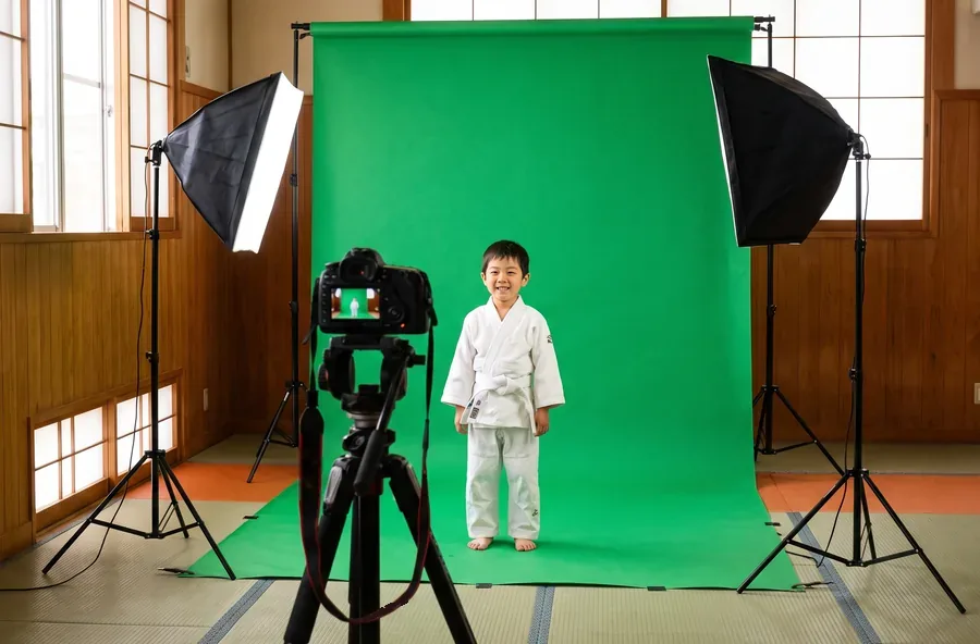Visuel d'illustration : un studio photo installé dans un dojo, avec fond vert, projecteurs et appareil sur pied ; un jeune judoka pose